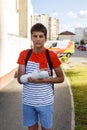 Teenage with broken hand in a cast in front of ambulance in the city. Boy in white t shirt holds his injured hand