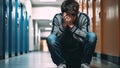 Teenage bullying sitting by locker against school corridor. Generative AI Royalty Free Stock Photo