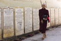 Teenage Burmese monk in dark purple robes holding bowl and walking barefoot