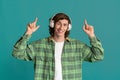 Teenage culture concept. Young man in headphones pointing upwards on color background