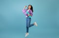 Teenage culture. Playful asian lady with skateboard jumping and having fun over blue studio background Royalty Free Stock Photo