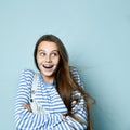 Teenage female in jeans overall, striped sweatshirt. She smiling, showing thumbs up, winking, posing on blue background. Close up