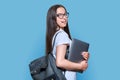 Teenage female student with backpack laptop on blue color background