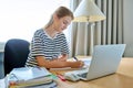 Teenage female student sitting at home at desk, writing in notebook using laptop computer Royalty Free Stock Photo