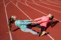 Teenage friends do partner stretch exercises on athletics track, friendship