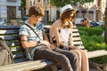 Teenage friends girl and boy sitting on bench in city, smiling, talking, looking in phone. Friendship and people concept Royalty Free Stock Photo