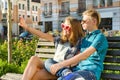 Teenage friends girl and boy sitting on the bench in the city, talking, looking in the phone, doing selfie photo Royalty Free Stock Photo