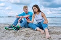 Teenage friends guy and girl sitting together on beach, talking looking at smartphone screen Royalty Free Stock Photo