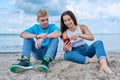 Teenage friends guy and girl sitting together on beach, talking looking at smartphone screen Royalty Free Stock Photo