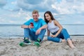 Teenage friends guy and girl sitting together on beach, talking looking at smartphone screen Royalty Free Stock Photo