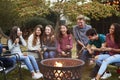 Teenage friends sit round a fire pit toasting marshmallows Royalty Free Stock Photo