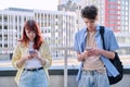Teenage friends guy and girl using smartphones, urban outdoor