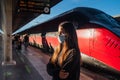 Teen girl at railroad station wearing a protective face mask looking at departure timetable board