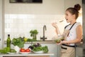 A teenage girl in apron prepared a salad on her own in the home kitchen. She holds a bowl of cooked salad and tastes it Royalty Free Stock Photo