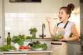 A teenage girl in apron prepared a salad on her own in the home kitchen. She holds a bowl of cooked salad and tastes it Royalty Free Stock Photo