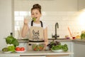 A teenage girl in apron prepared a salad on her own in the home kitchen. She holds a bowl of cooked salad and tastes it Royalty Free Stock Photo