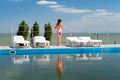 Teenage girl in bathing suit stands between sun loungers by pool background sea Royalty Free Stock Photo