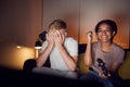 Teenage Girl Beating Boy As They Sit On Sofa At Home Playing Computer Game