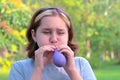 A teenage girl began to inflate a lilac balloon in nature in the park