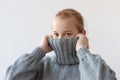 A teenage girl with blonde hair pulled the collar of a gray sweater over her face with her hands, only her eyes are visible Royalty Free Stock Photo