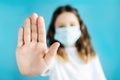 Teenage girl in a blue medical mask, white t-shirt holds out her hand forward making a stop sign on a blue background Royalty Free Stock Photo