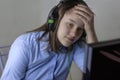 A teenage girl in a blue shirt and headphones looks at the computer monitor, holding her forehead with her hand. Concept of online Royalty Free Stock Photo