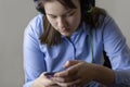 A teenage girl in a blue shirt and headphones looks at the phone in her hands. Concept of online learning, distance learning, Royalty Free Stock Photo