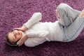 A young girl lies on her back on the carpet and listens to music on headphones.