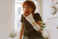 teenage girl with broken arm in cast in kitchen sitting on countertop eating apple