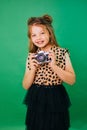 Teenage girl in colorful clothes on a green background with an adorable smile. The child holds a camera in his hands