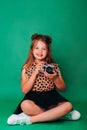 Teenage girl in colorful clothes on a green background with an adorable smile. The child holds a camera in his hands