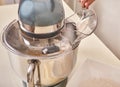 A teenage girl cooks a homemade cake in the kitchen. Mixes the ingredients for the cake in an electric mixer. The hand