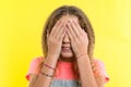 Teenage girl with curly blond hair covered her face with hands, bright yellow studio background Royalty Free Stock Photo