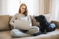 Teenage girl with a dog sitting on a sofa indoors, working on a laptop. Royalty Free Stock Photo