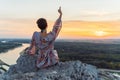 teenage girl in dress, with short-cropped hair, on top cliff, on river bank, at sunset Royalty Free Stock Photo