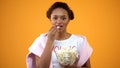 Teenage girl enjoying comedy series on tv eating popcorn on orange background