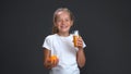 Teenage girl enjoys a glass of orange juice holding fresh orange in other hand. Healthy food concept. Isolated on gray Royalty Free Stock Photo