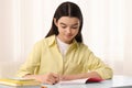 Teenage girl erasing mistake in her notebook at white desk indoors