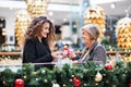 A teenage girl giving present to grandmother in shopping center at Christmas. Royalty Free Stock Photo