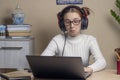 Teenage girl with glasses and headphones is studying on laptop. cute teenage girl is surprised to listen to something Royalty Free Stock Photo