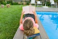 Teenage girl in glasses reads a book, background swimming pool, lawn near the house. School, education, knowledge, adolescents.