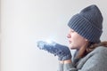 A teenage girl in a gray knitted hat, sweater and mittens holds a small bright star in her hands and blows on it Royalty Free Stock Photo