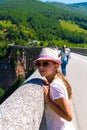 A teenage girl in a hat and glasses on the bridge looking out into the distance against the background of the mountains. Royalty Free Stock Photo