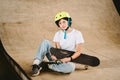 Teenage girl in helmet and stylish clothes posing on half pipe ramp an outdoor skate park. Beautiful kid female model skateboarder Royalty Free Stock Photo