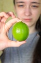 A teenage girl holds a whole green lime in her hand with her fingers. blurry Royalty Free Stock Photo