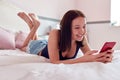 Teenage Girl At Home Using Mobile Phone Lying On Bed In Bedroom Royalty Free Stock Photo