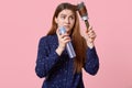 Teenage girl hurries for date, tries to make hairstyle, combs hair with hairbrush, uses hairspray, dressed in shirt, poses over