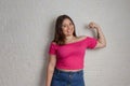 Teenage girl in inspirational pose showing flexed arms. Isolated on white brick wall