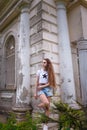 Teenage girl in jeans shorts and white T-shirt with star design and long curly hair posing at some building