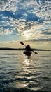 teenage girl is kayaking Pelican at sunset in Pacific Ocean only silhouette of Kayak Paddles is visible she swims sunny